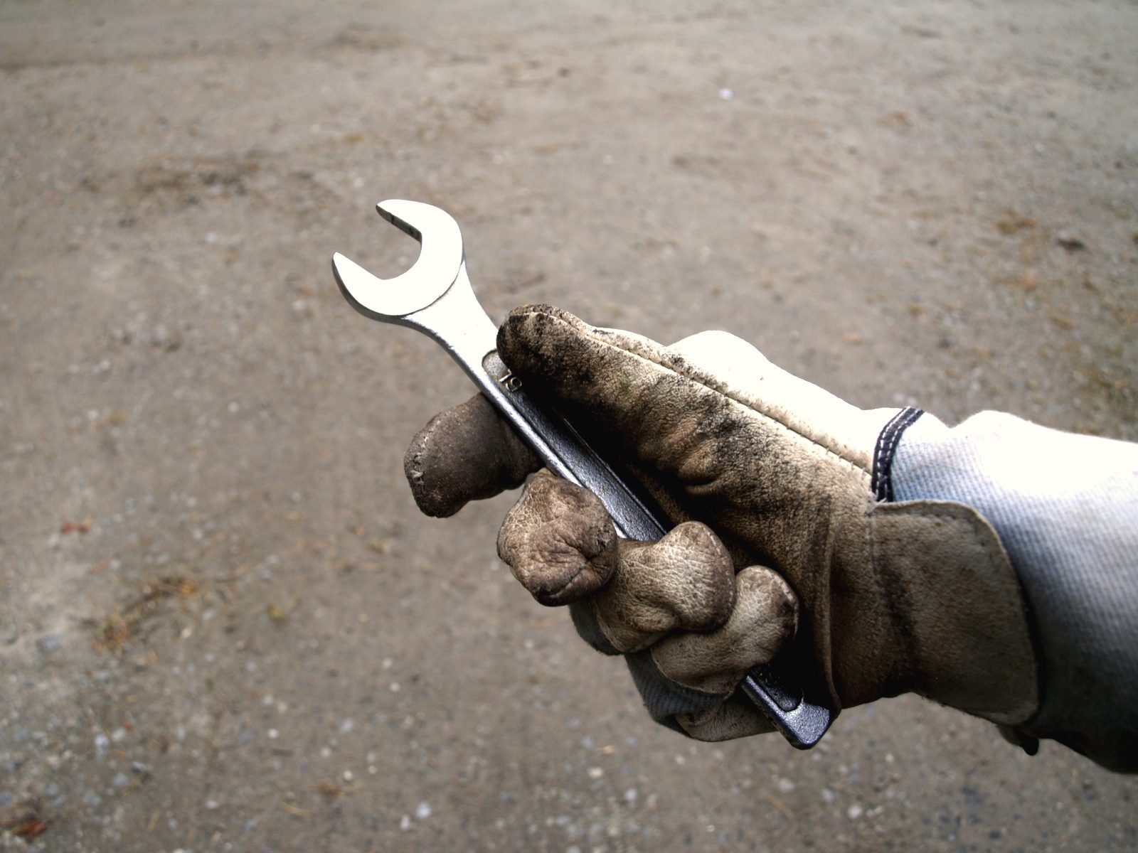 A gloved hand holding an adjustable wrench over concrete