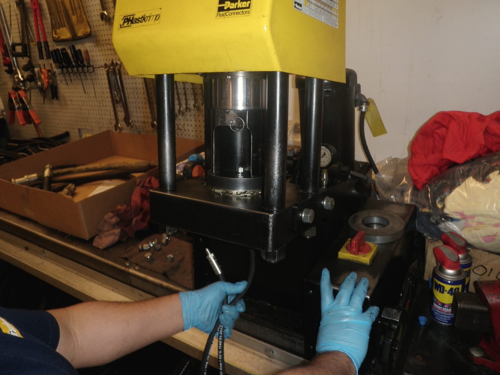 Gloved hands loading a hose fitting into a bench crimping machine