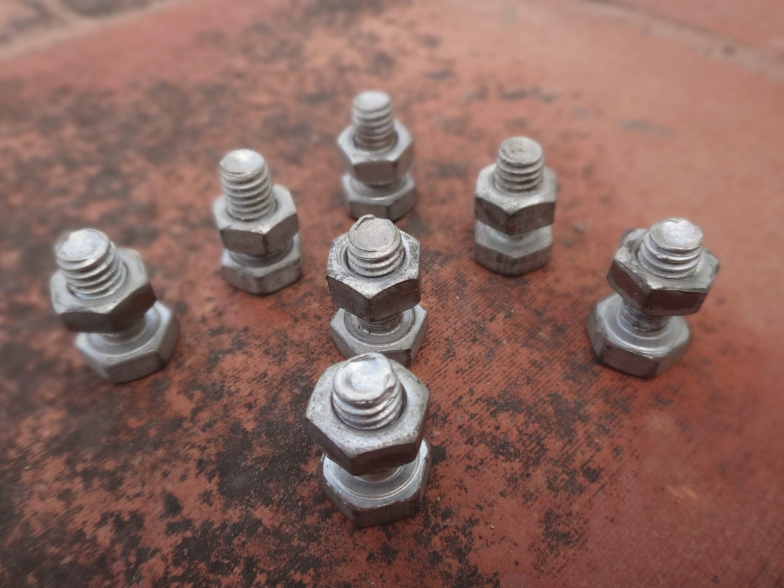 Short bolts with nuts threaded on, standing on a rusty steel plate