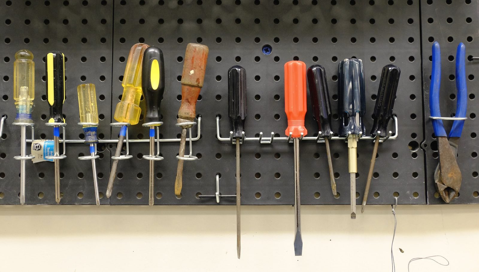 A row of screwdrivers and a pair of pliers hanging on pegboard