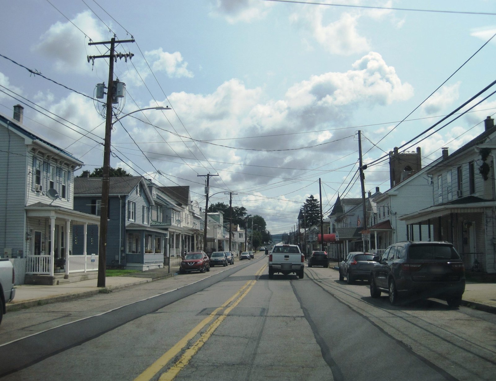 Route 209 through Tower City, Pennsylvania, with rowhouses and porches along both sides and a wooded ridge behind